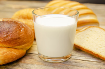 Glass of milk, rolls, sliced loaf on a wooden background