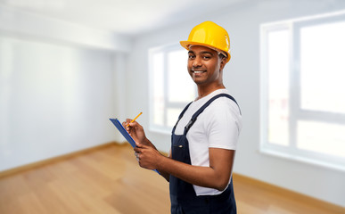 profession, construction and building - happy smiling indian worker or builder in helmet with clipboard and pencil over empty room at new home or apartment background