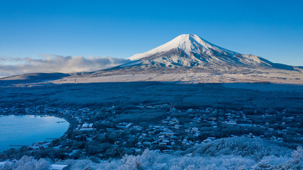Fototapeta na wymiar Aerial view of Mount Fuji in winter, iconic snow-capped symbol of Japan, snow covered scenery with freezing fog on trees, lake Yamanaka, clear blue sky - landscape panorama of Japan from above, Asia
