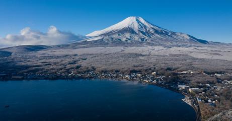 Aerial view of Mount Fuji in winter, iconic snow-capped symbol of Japan, snow covered scenery with freezing fog on trees, lake Yamanaka, clear blue sky - landscape panorama of Japan from above, Asia