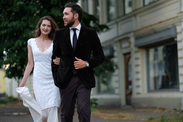Beautiful wedding couple of newlyweds - red-haired young bride in a white dress and a bearded groom in a black suit. Amazing smiling wedding couple. Pretty bride and stylish groom.