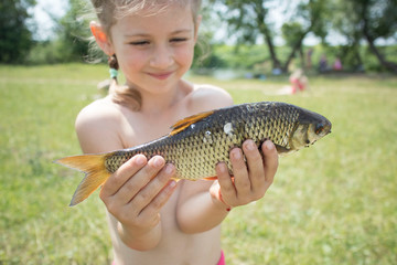 girl holds a live fish on the beach in summer Sunny weather