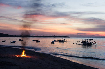 Atardecer relajante en una playa de Bali con barcas y hoguera