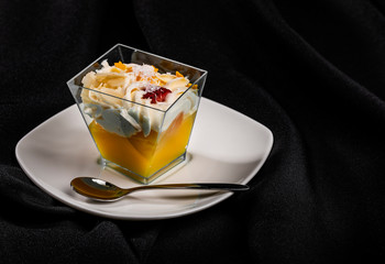 Individual portion of double-layered dessert in trapezoid clear bowl on white saucer with teaspoon