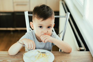 A child in the kitchen at the table eats macaroni and cheese very appetizing