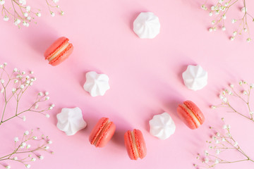 Pink macarons, white marshmallows and flowers on a pink pastel background.