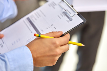 business, people and statistics concept - close up of businessman's hands holding pencil and clipboard with bill
