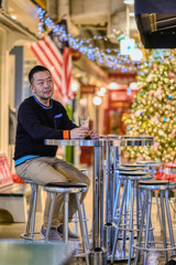 Fototapeta premium A young Asian man sits at a table in a cafe with a beer glass, with Christmas decorations in the background