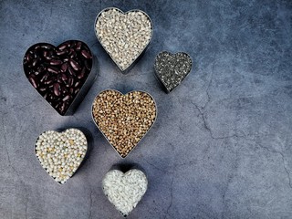 Obraz premium Grain and cereal food selection in heart shaped bowls on dark background. Top view. 
