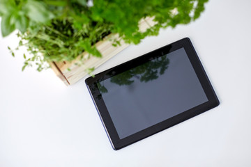 gardening, plants and organic concept - tablet pc computer with herbs and flowers in wooden box on table