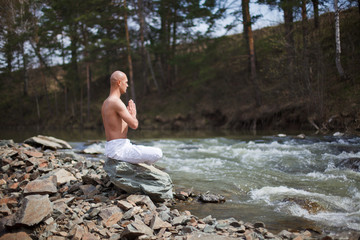 Buddhist. Bald man. Meditation in the mountains against the backdrop of a waterfall. Prayer.
