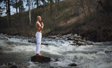 Buddhist. Bald man. Meditation in the mountains against the backdrop of a waterfall. Prayer.