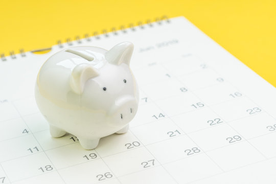 Finance, saving money or salary pay day, white piggy bank on white clean calendar on solid yellow background