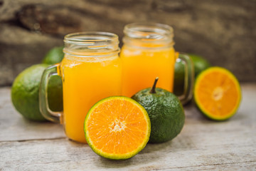 Orange juice and oranges with green peel on a wooden background