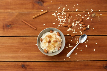 food and breakfast concept - oatmeal porridge in bowl with sliced banana, almond nuts and cinnamon on wooden table