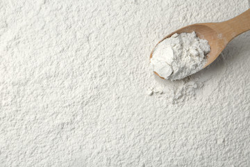 Wooden spoon on wheat flour, top view. Space for text