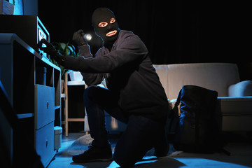 Thief with flashlight near steel safe indoors at night - obrazy, fototapety, plakaty