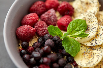 food and breakfast concept - close up of cereals in bowl with wild berries, banana and peppermint on slate stone table
