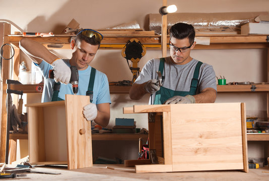 Professional carpenters assembling wooden cabinet in workshop