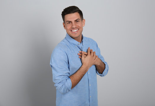 Handsome Grateful Man With Hands On Chest Against Light Grey Background