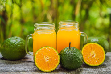 Orange juice and oranges with green peel on a wooden background