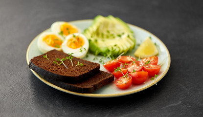 food, eating and breakfast concept - toast bread with cherry tomatoes, avocado, eggs and greens on ceramic plate