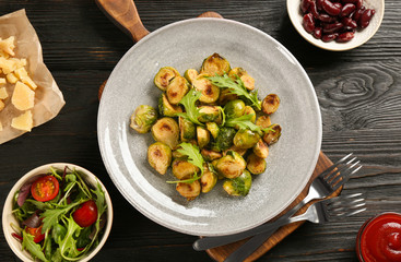 Delicious roasted brussels sprouts with arugula served on black wooden table, flat lay