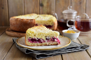 A piece of cherry pie on a white plate in the foreground, a Cup of tea and a teapot of tea in the background