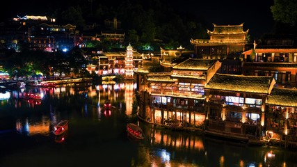 Fototapeta na wymiar Night scenery view of ancient Chinese town Fenghuang County with illuminated buildings and boats. Hunan, China