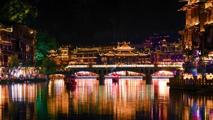 Night scenery view of ancient Chinese town Fenghuang County with illuminated buildings and bridge. Hunan, China