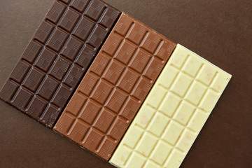 sweets, confectionery and food concept - milk, dark and white chocolate bars on brown background