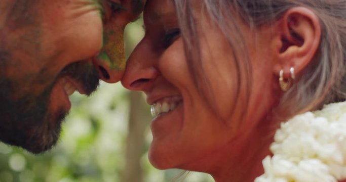 Extreme close-up of caucasian couple, smile, joy, laugh, taking wedding vows in Hindu tradition as they wear floral garlands and hug covered in holi colors, as they are declared husband and wife 60fps