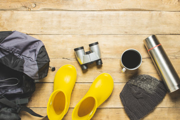 Yellow rain boots, backpack, binoculars, camping equipment on a wooden background. The concept of...