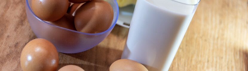 A glass of milk and beside it a piece of cheese and eggs on a wooden background