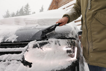 Young man cleaning snow from car outdoors on winter day, closeup
