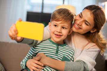 family, love and people concept - happy smiling mother with little son taking selfie by smartphone at home in evening