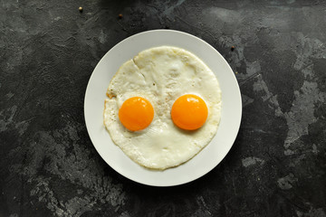 Fried eggs in a plate isolated. Beautiful fried eggs. Tasty breakfast. Top view, dark concrete background.