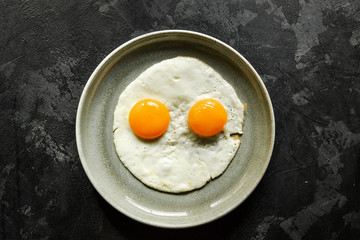 Fried eggs in a plate isolated. Beautiful fried eggs. Tasty breakfast. Top view, dark concrete background.