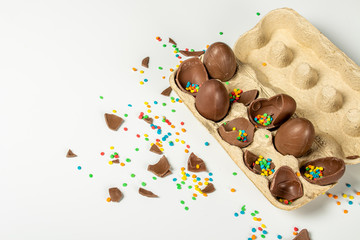Tray with broken Easter chocolate eggs and multi-colored sweet candy decorations on a light background. Easter concept, easter treats, bunny. Banner