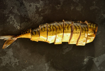 Cold smoked mackerel. Smoked fish. A whole fish on a dark background, cut into pieces. Top view, place for text.
