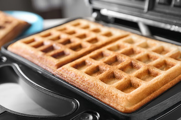 Modern iron with tasty Belgian waffles on table, closeup