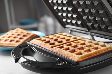 Modern iron with tasty Belgian waffles on table, closeup