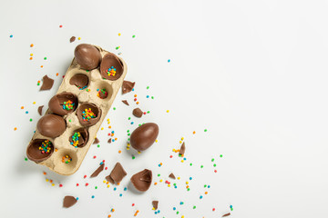 Tray with broken Easter chocolate eggs and multi-colored sweet candy decorations on a light background. Easter concept, easter treats, bunny. Banner. Flat lay, top view