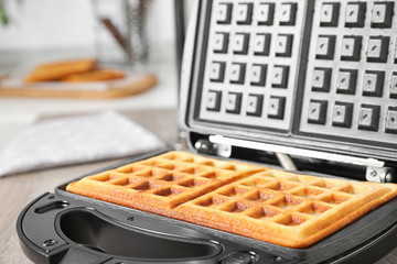Modern iron with tasty Belgian waffles on table, closeup
