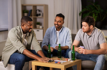 leisure games, friendship and gambling concept - happy male friends playing cards and drinking beer at home at night