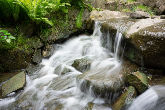 time exposure photo shot with a small waterfall over rocks in a stream and milky blurred water