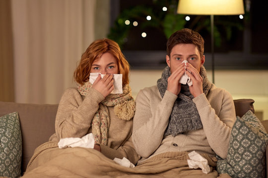 health, flu and people concept - sick young couple with tissue blowing nose at home