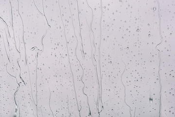 Raindrops background. Flowing water from the surface of the window. Raindrops and jets on a gray background of clouds.