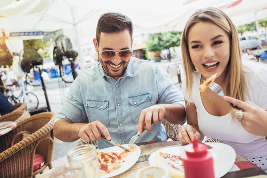 Couple eating pizza outdoors and smiling.They are sharing pizza in a outdoor cafe.
