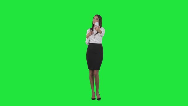 Young beautiful business woman taking selfies and using cellphone as mirror. Full body on chroma key green screen background.